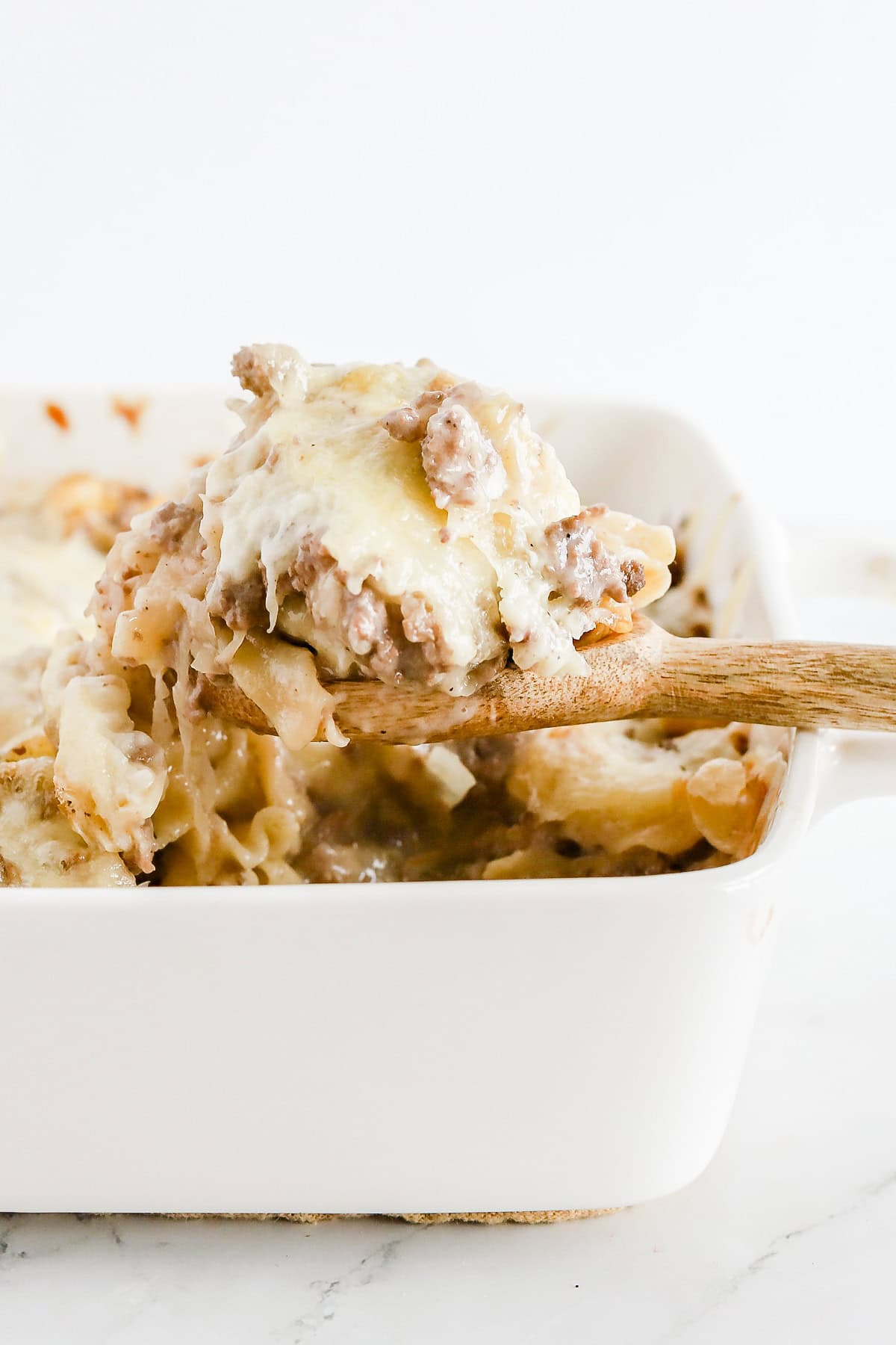 Wooden spoon scooping sauerkraut casserole out of white baking dish.