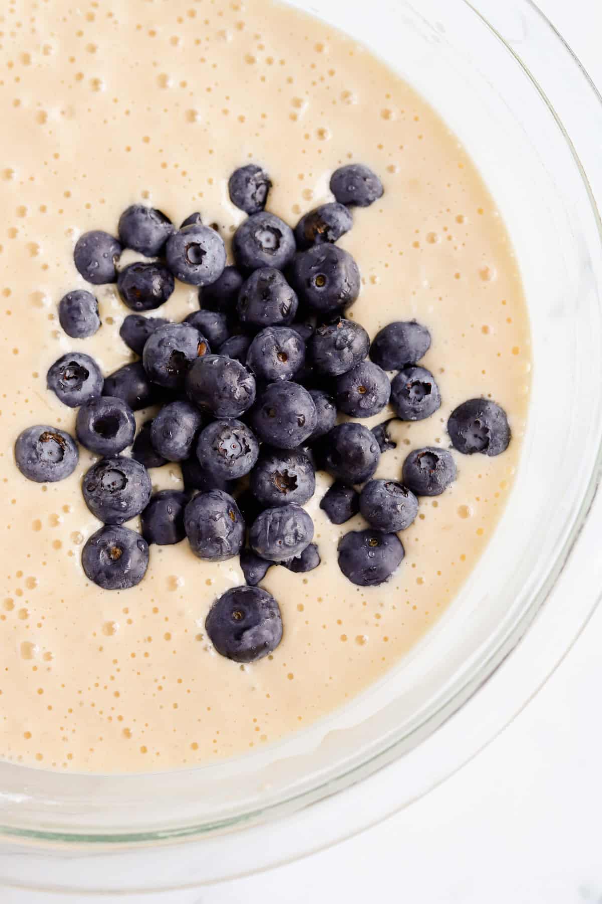 Fresh blueberries added to pancake batter in a glass bowl.