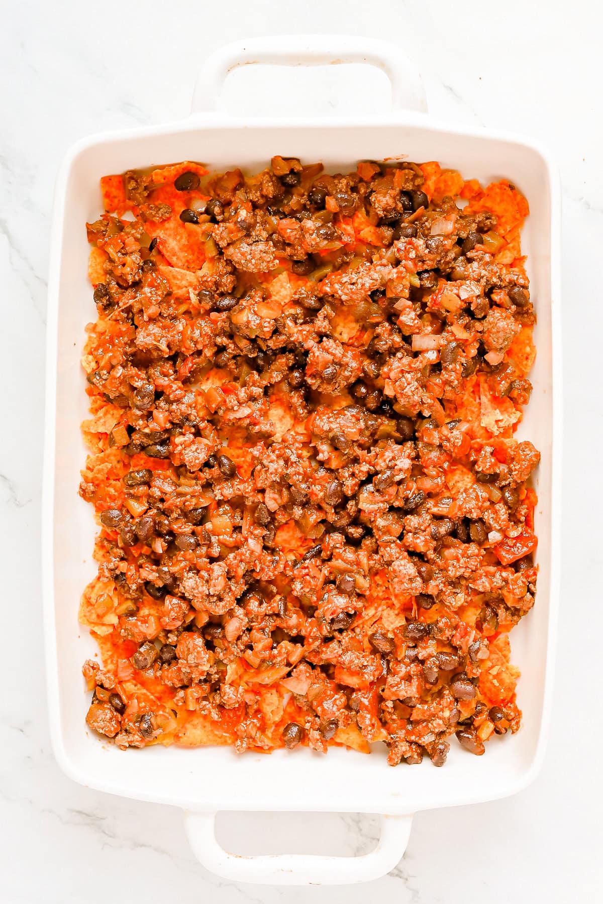 Seasoned meat added to baking dish with Doritos.