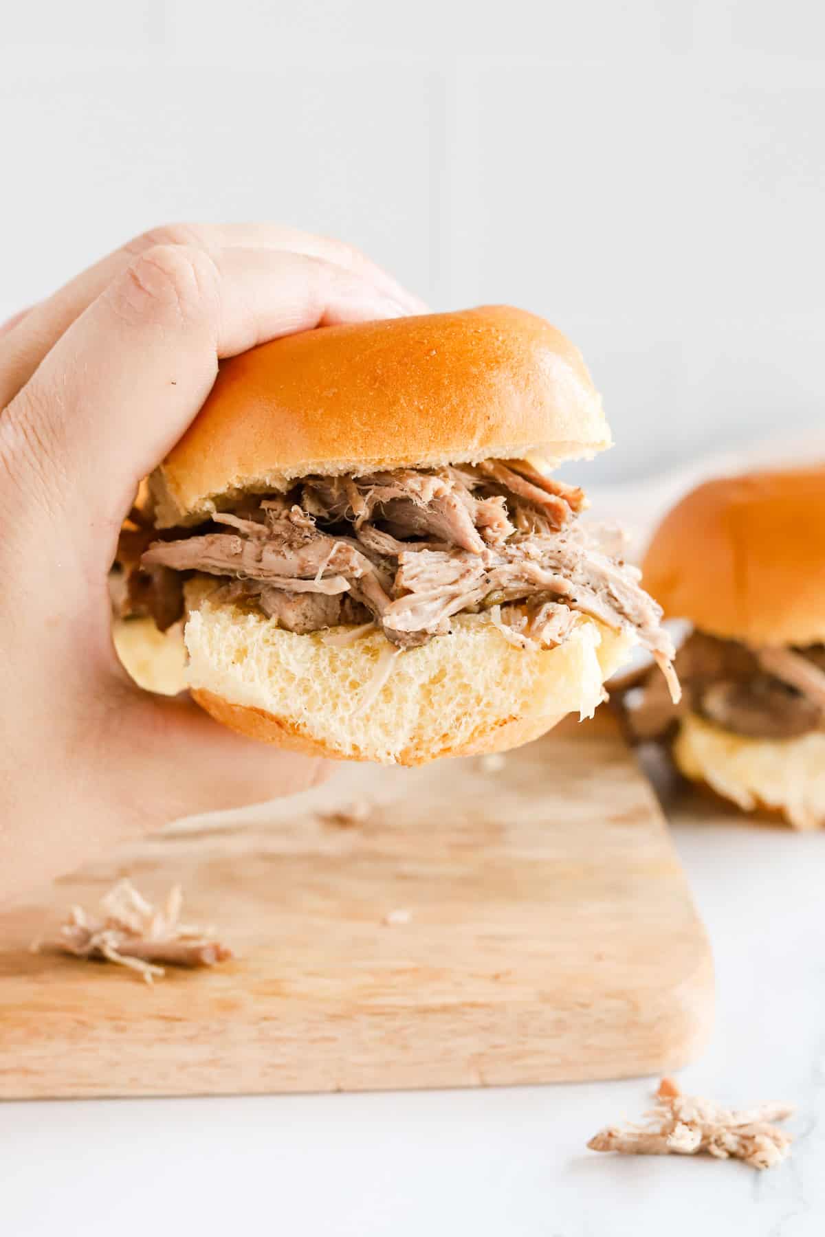 hand holding a porketta sandwich on a small brioche bun.