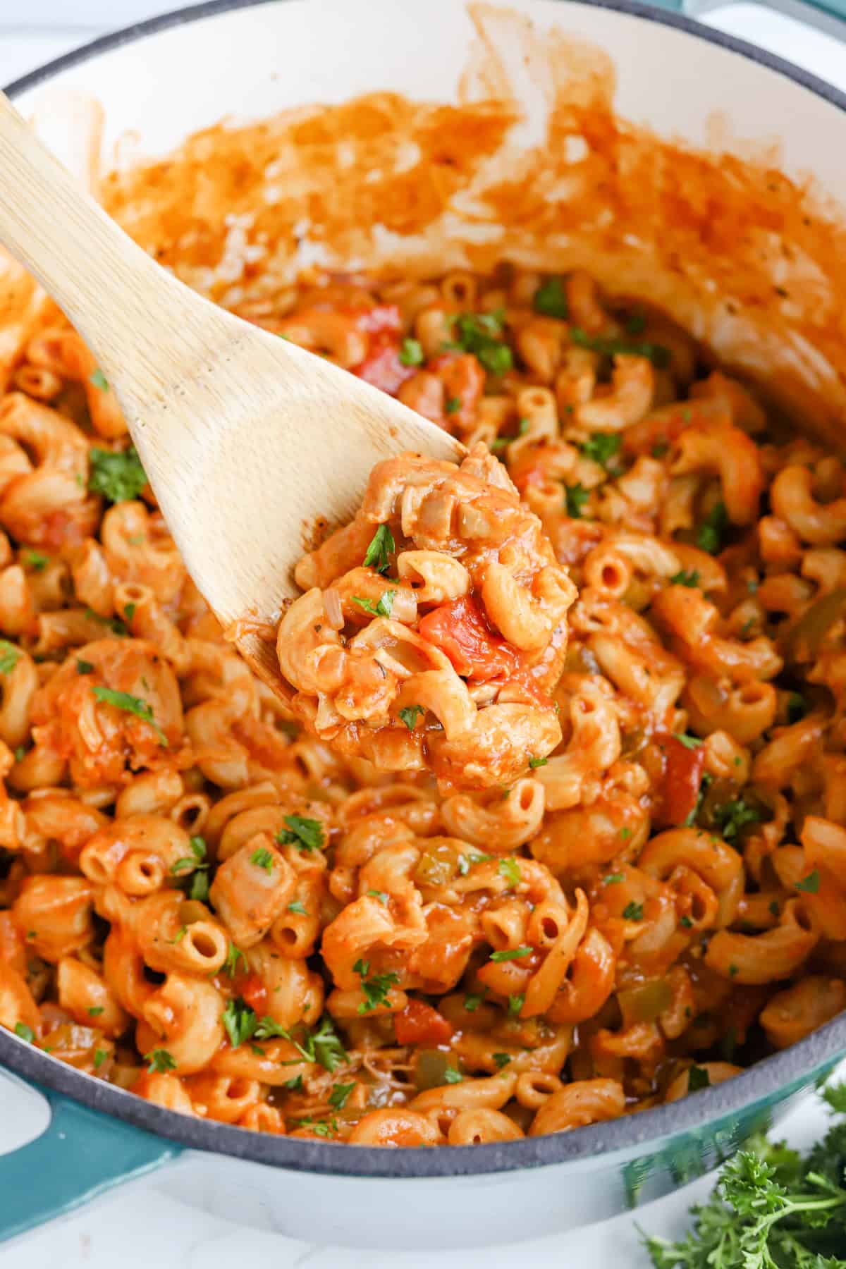 Wooden spoon lifting a scoop of chicken goulash out of the dutch oven.