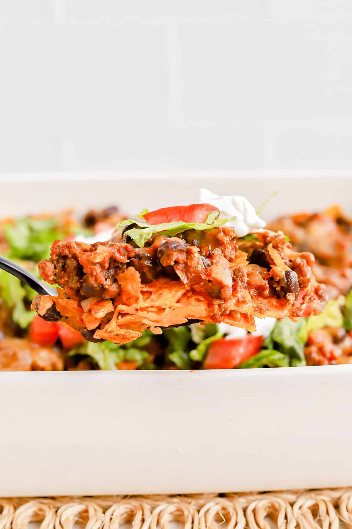 Spoon lifting a scoop of walking taco casserole out of white baking dish.
