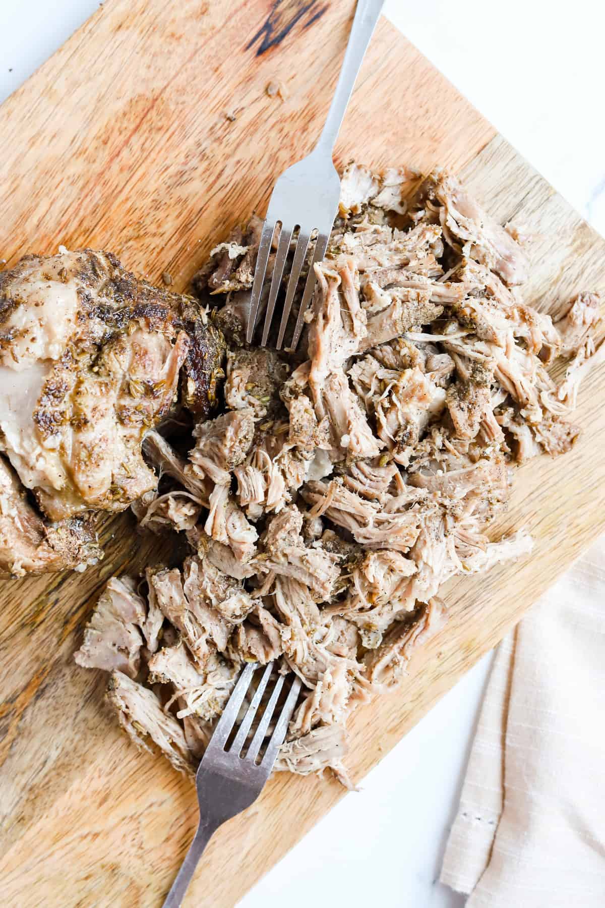 Shredded porketta on a wooden cutting board with two forks.