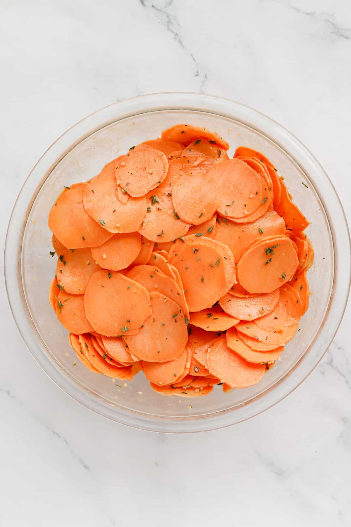 Bowl of thinly sliced sweet potatoes tossed in a seasoned butter mixture.