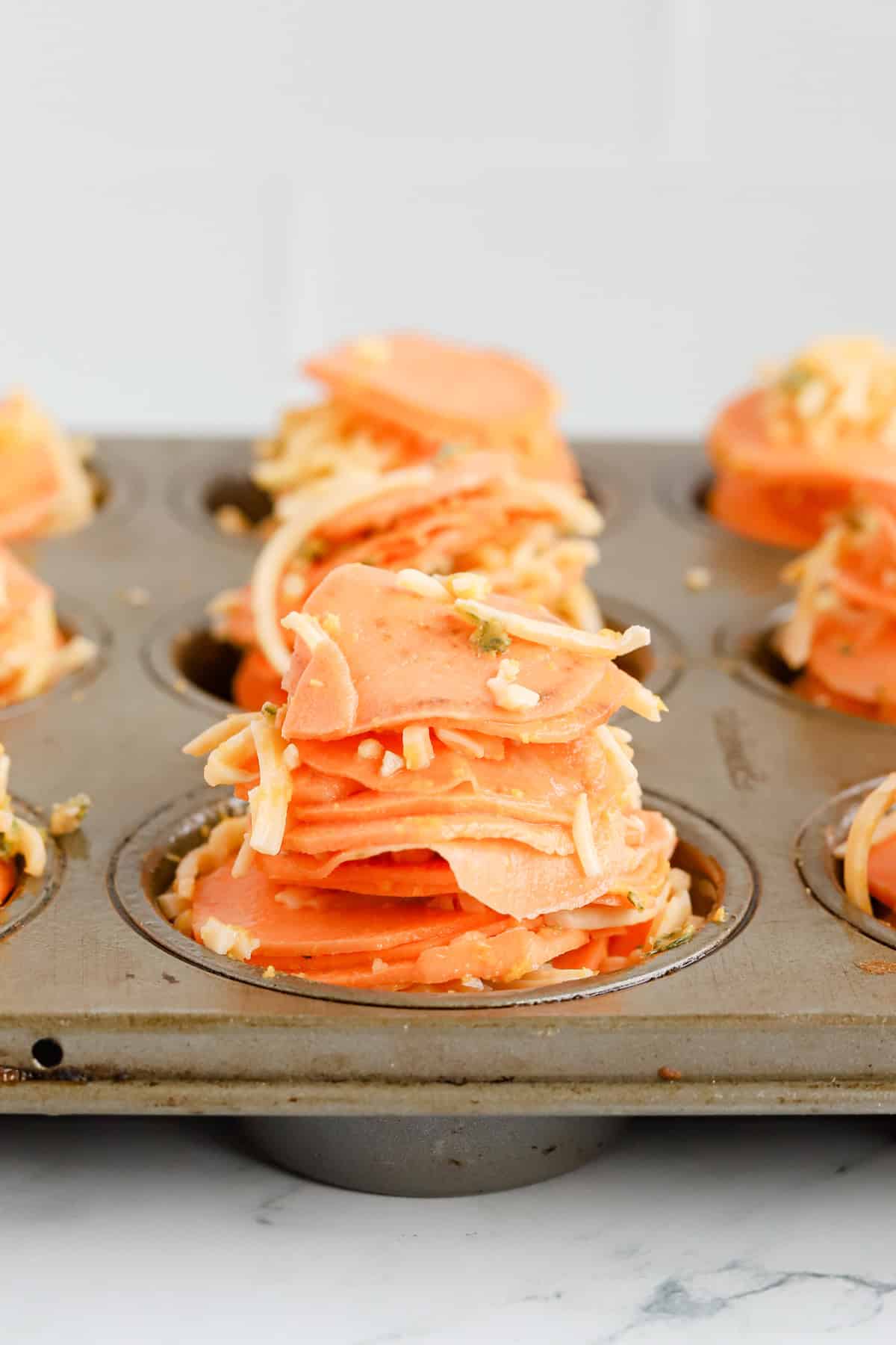 Raw sweet potato slices with seasonings and cheese stacked tall in muffin tin