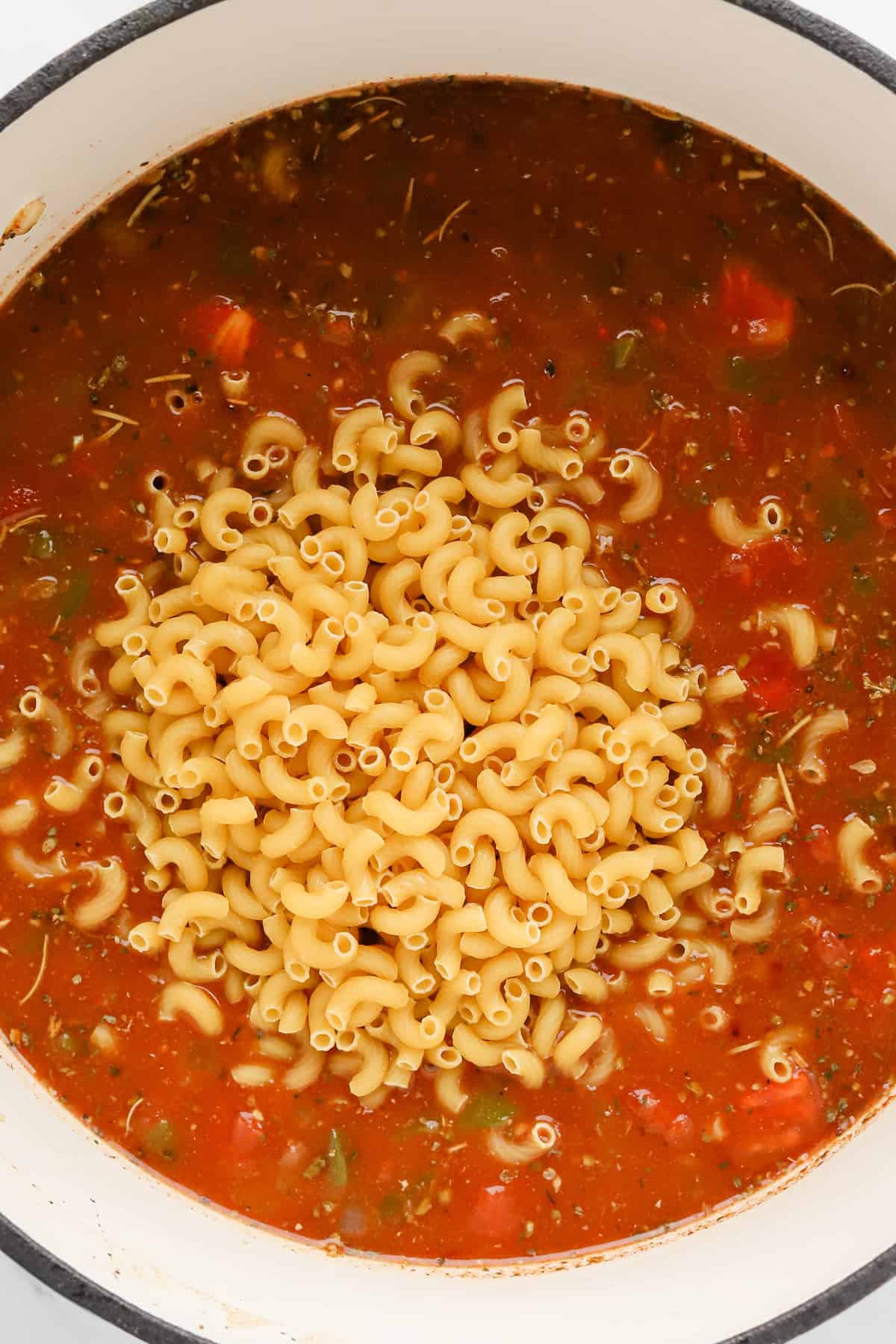 Uncooked elbow macaroni added to tomato broth mixture to cook.