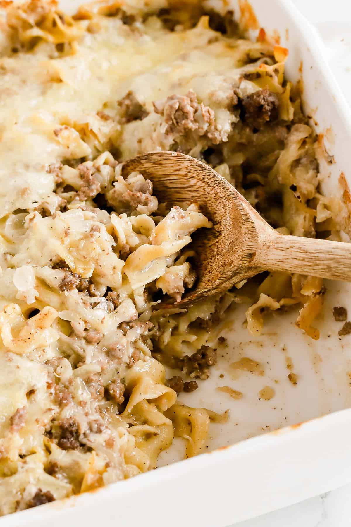Wooden spoon resting in baking dish of casserole with some taken out.