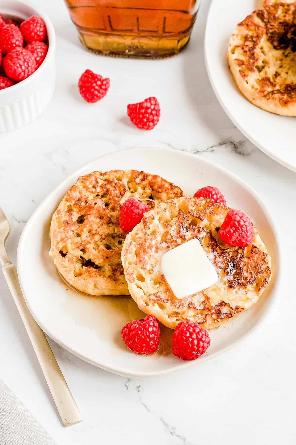 2 pieces of French toast with butter, syrup and raspberries on a white plate