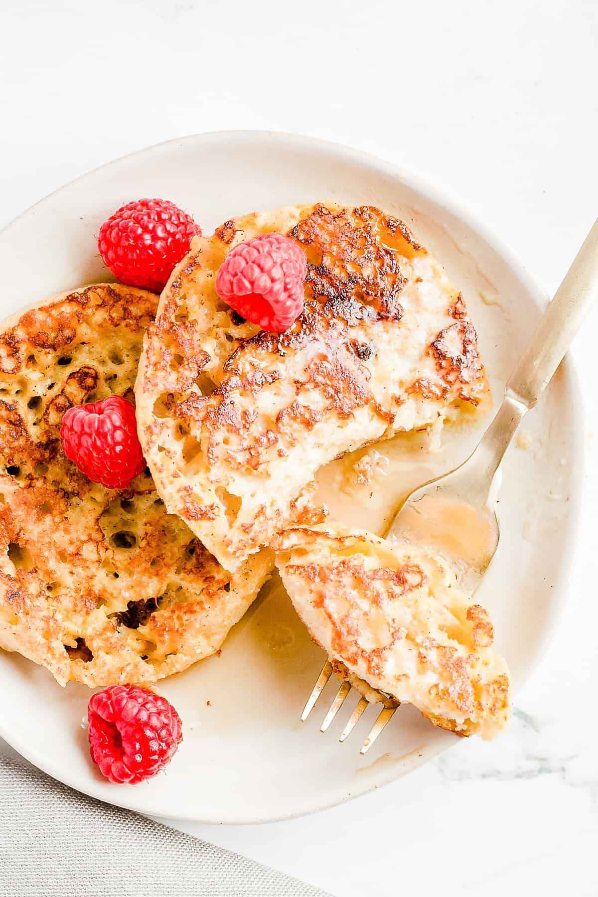 2 pieces of French toast on white plate with syrup and raspberries and a small piece on a fork