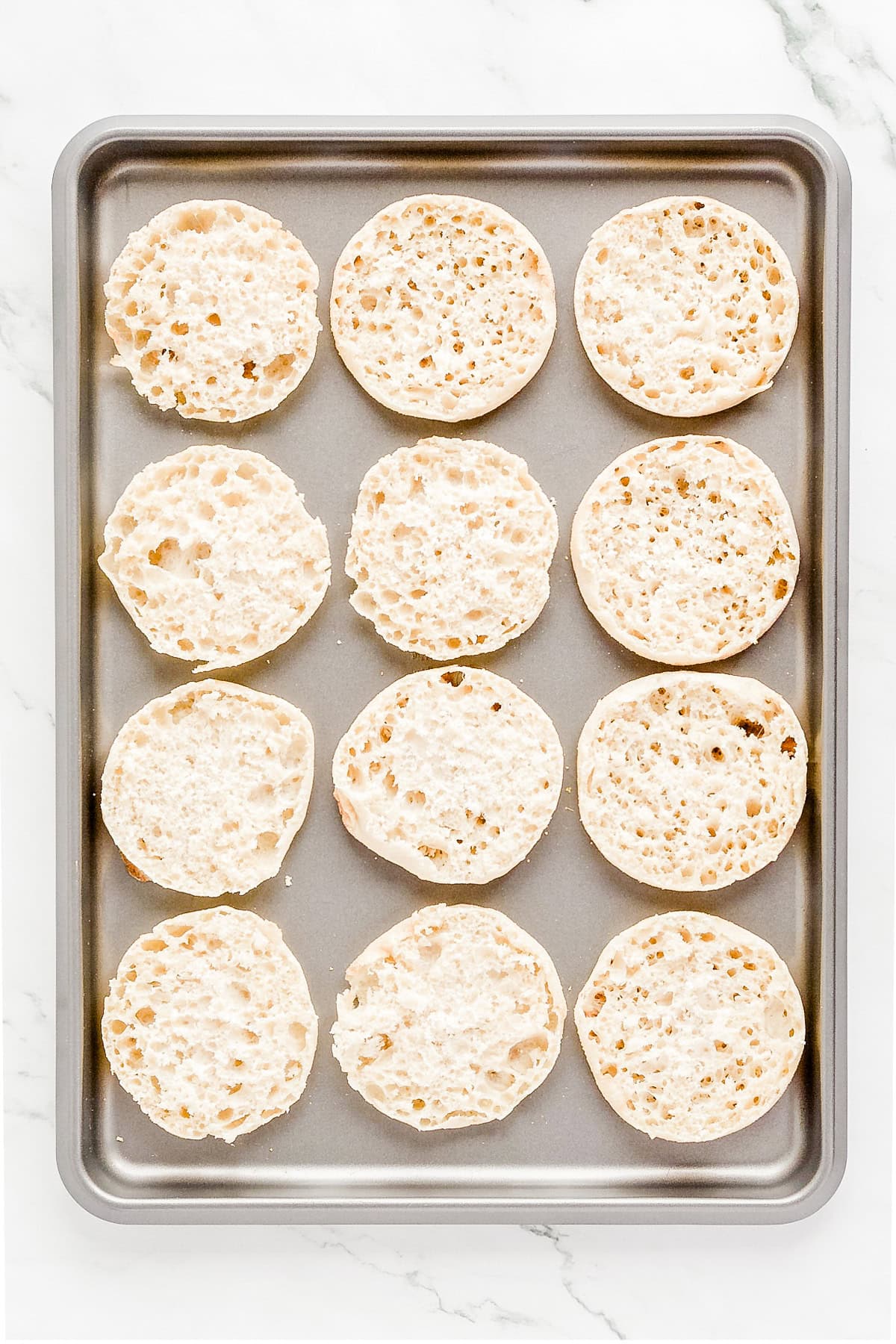 Halved English muffins on a sheet pan.