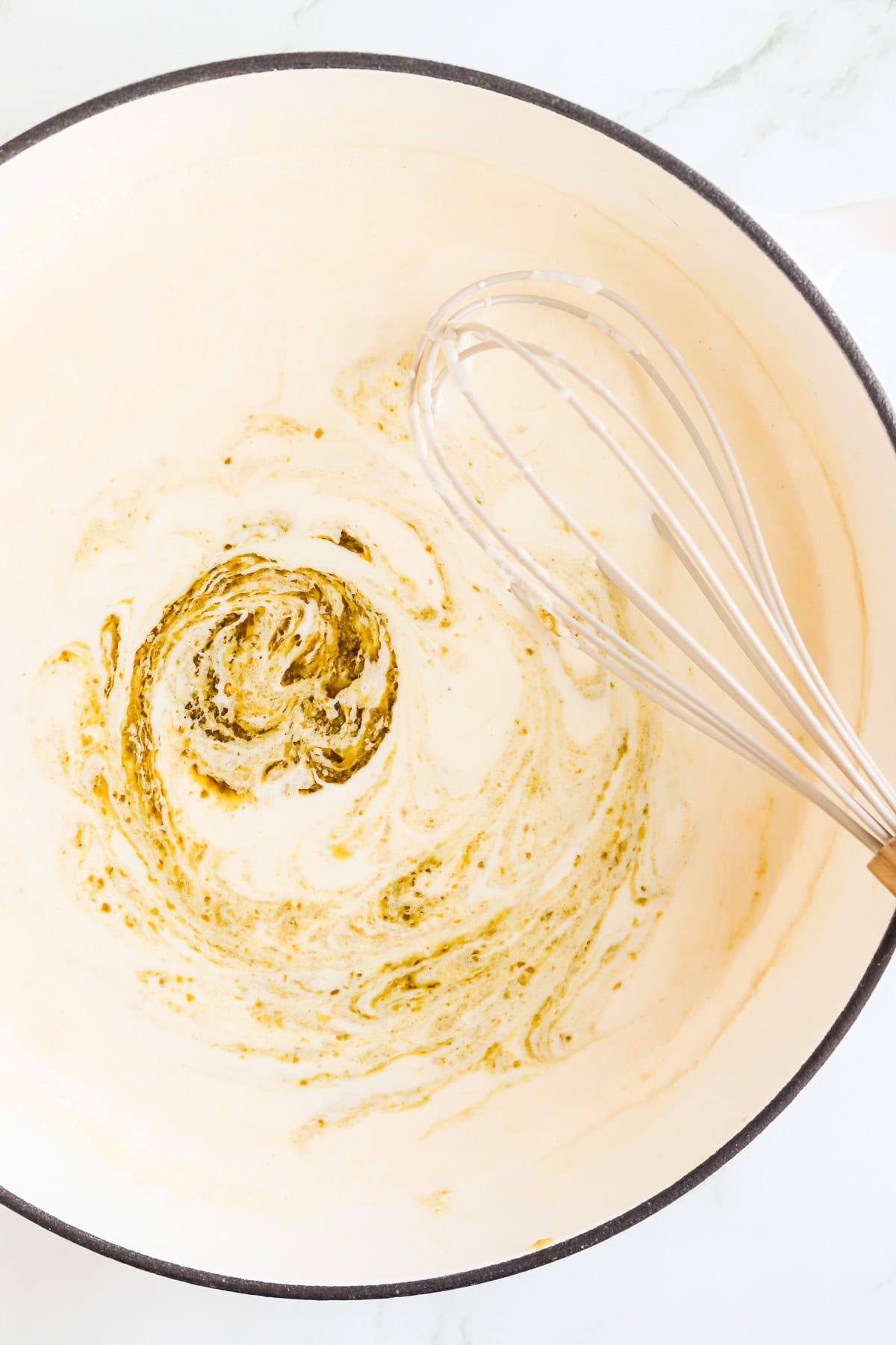 Swirl of store-bought pesto in Alfredo sauce with a whisk.