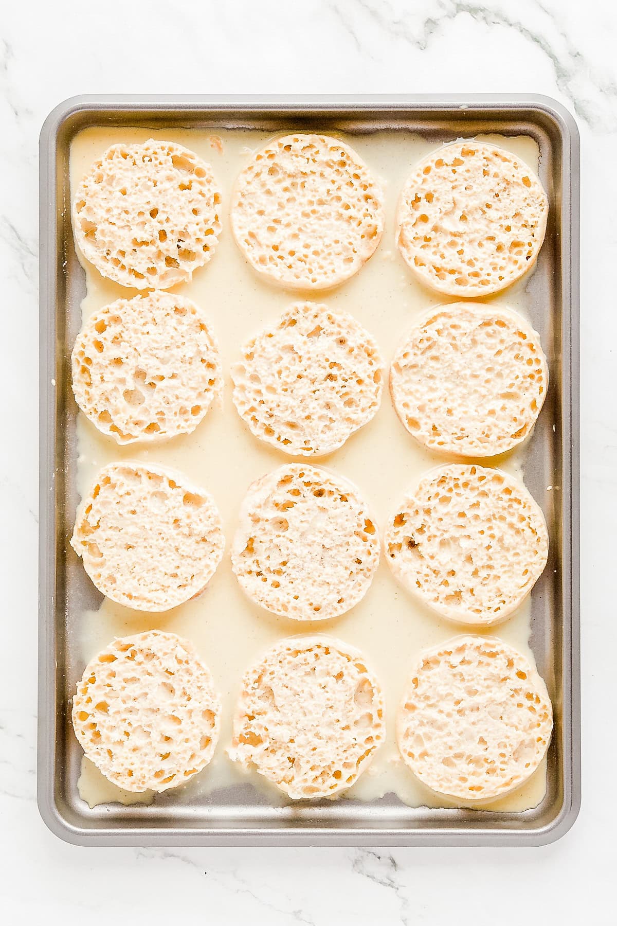 Custard poured over rimmed sheet pan with English muffins.