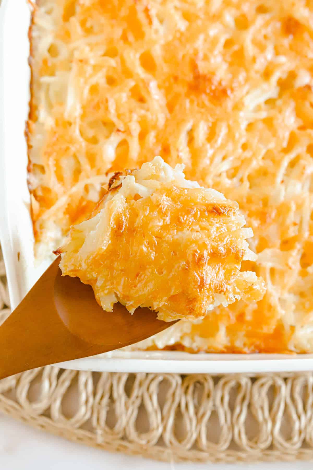 Wooden spoon with a scoop of cheesy potatoes held above baking dish.