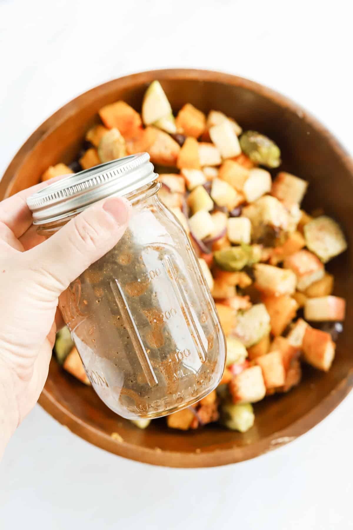 Hand holding a mason jar of balsamic vinaigrette above wooden bowl of panzanella salad