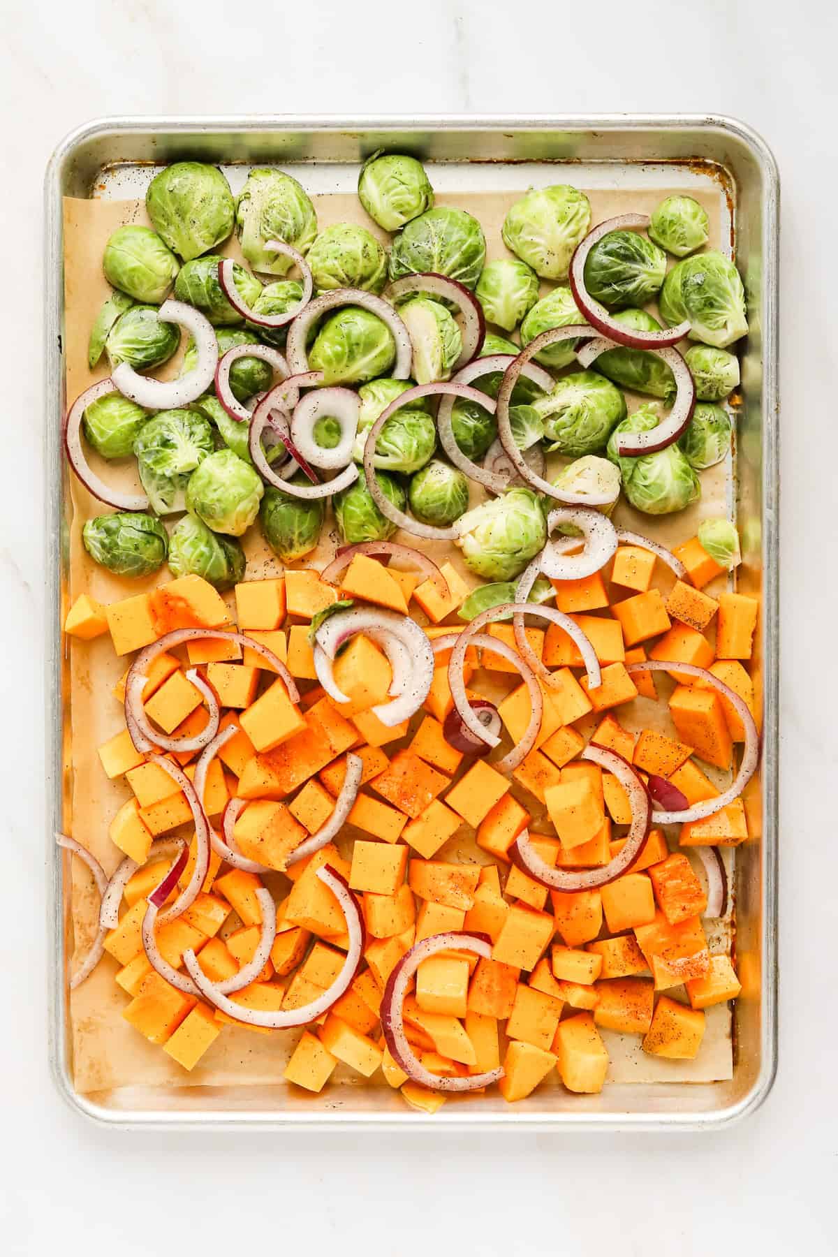 Sheet pan with raw Brussels sprouts, diced butternut squash and sliced red onion.