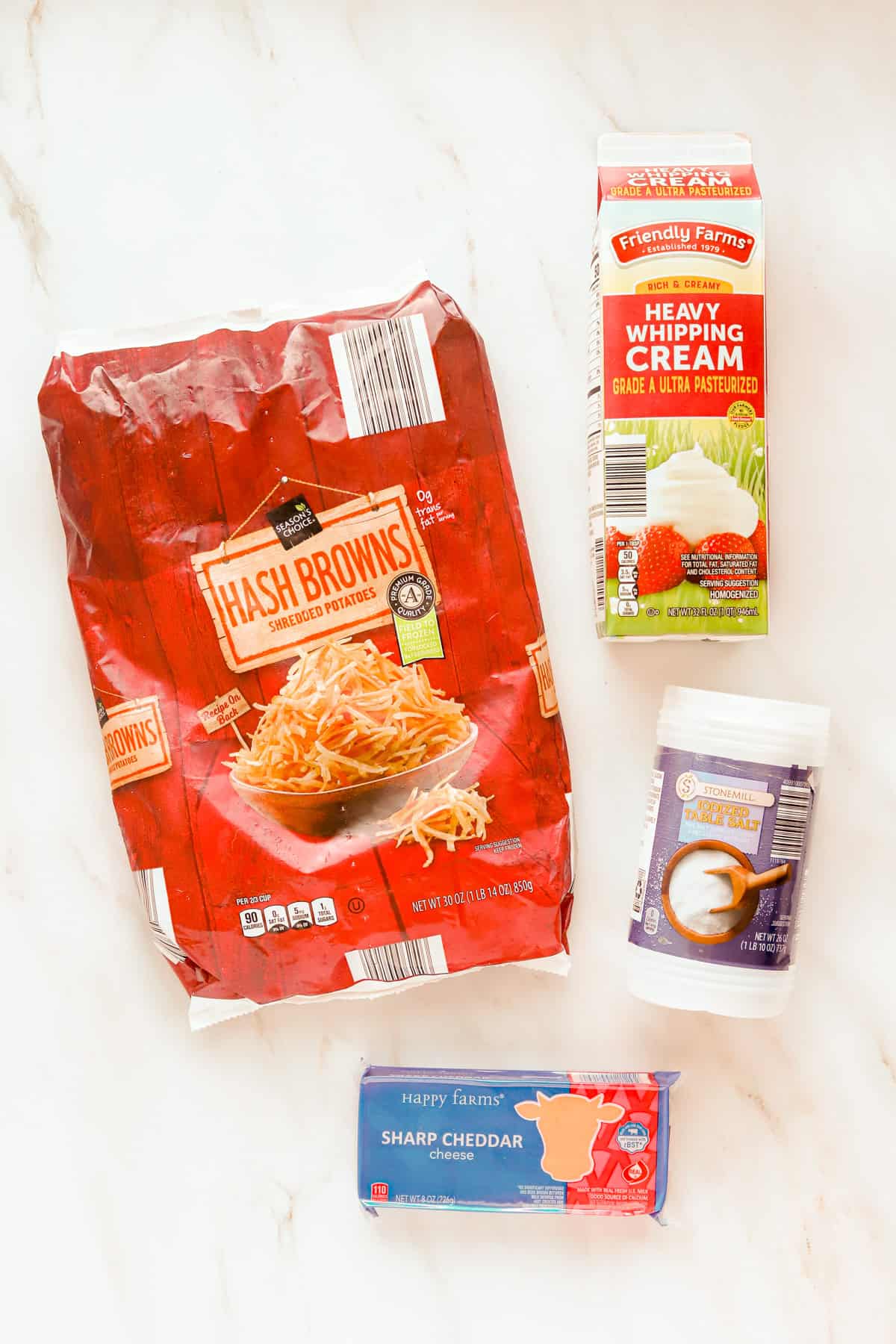 Bag of thawed hash browns, carton of heavy cream, container of salt and block of sharp cheddar on countertop.