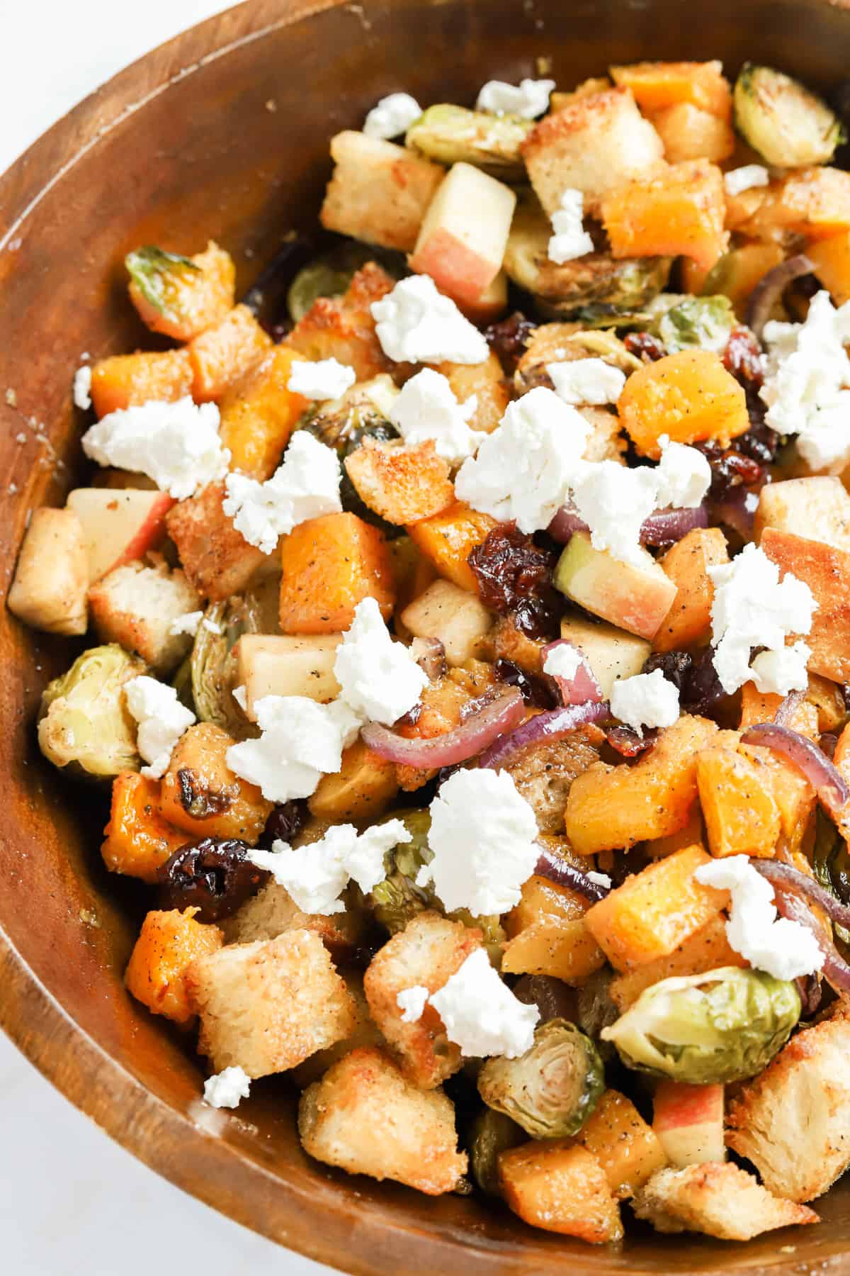 Close up of goat cheese dolloped on top of panzanella salad in wooden bowl.