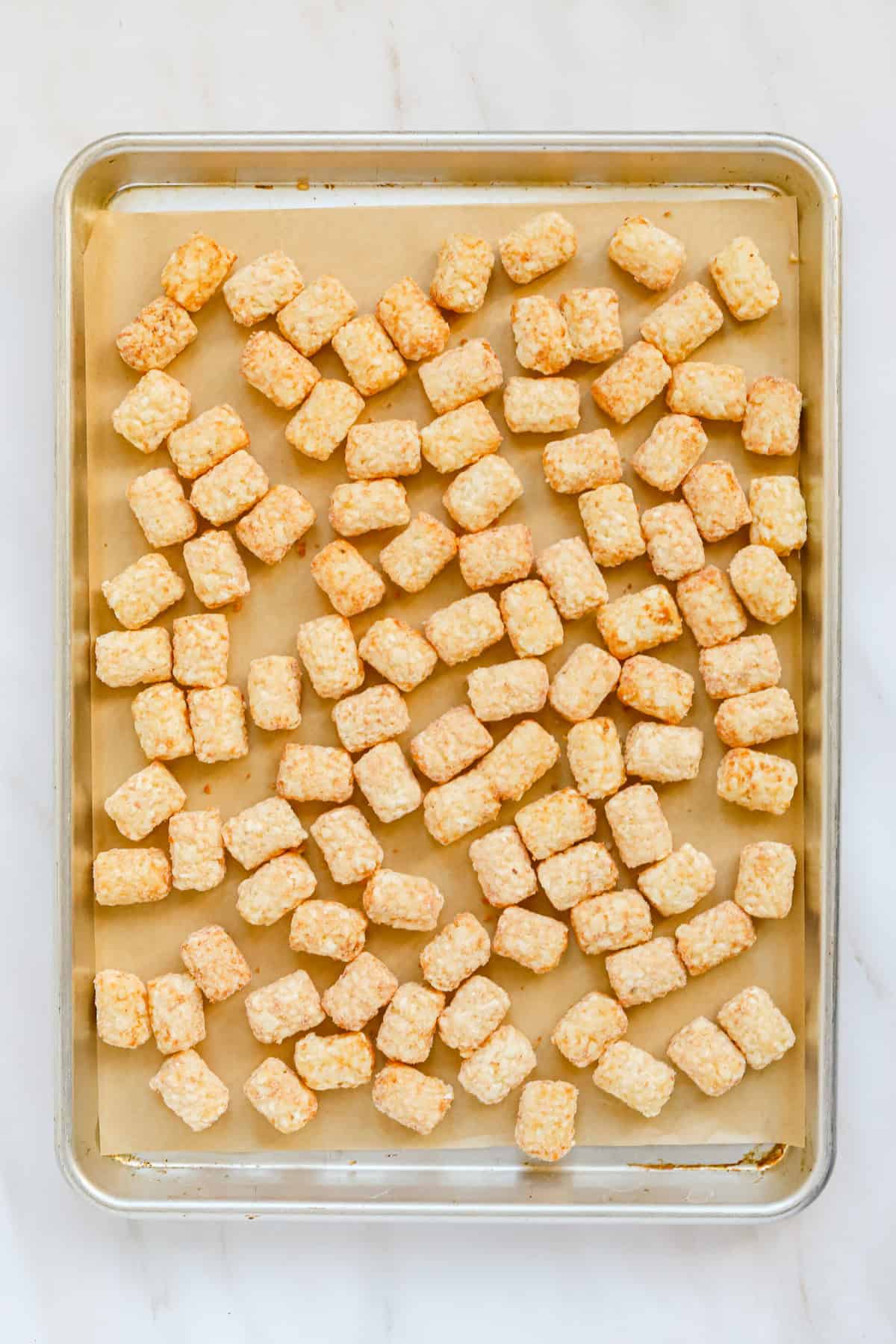 Frozen tater tots on parchment lined sheet pan.