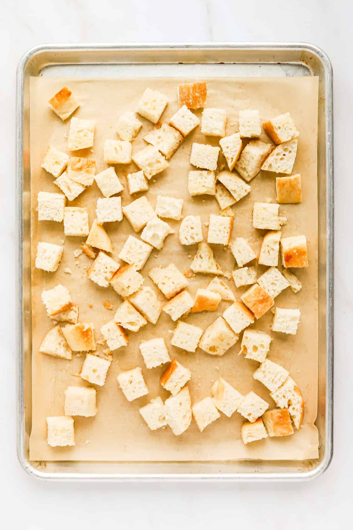 Cubed italian bread coated in olive oil, butter and garlic powder on a sheet pan.