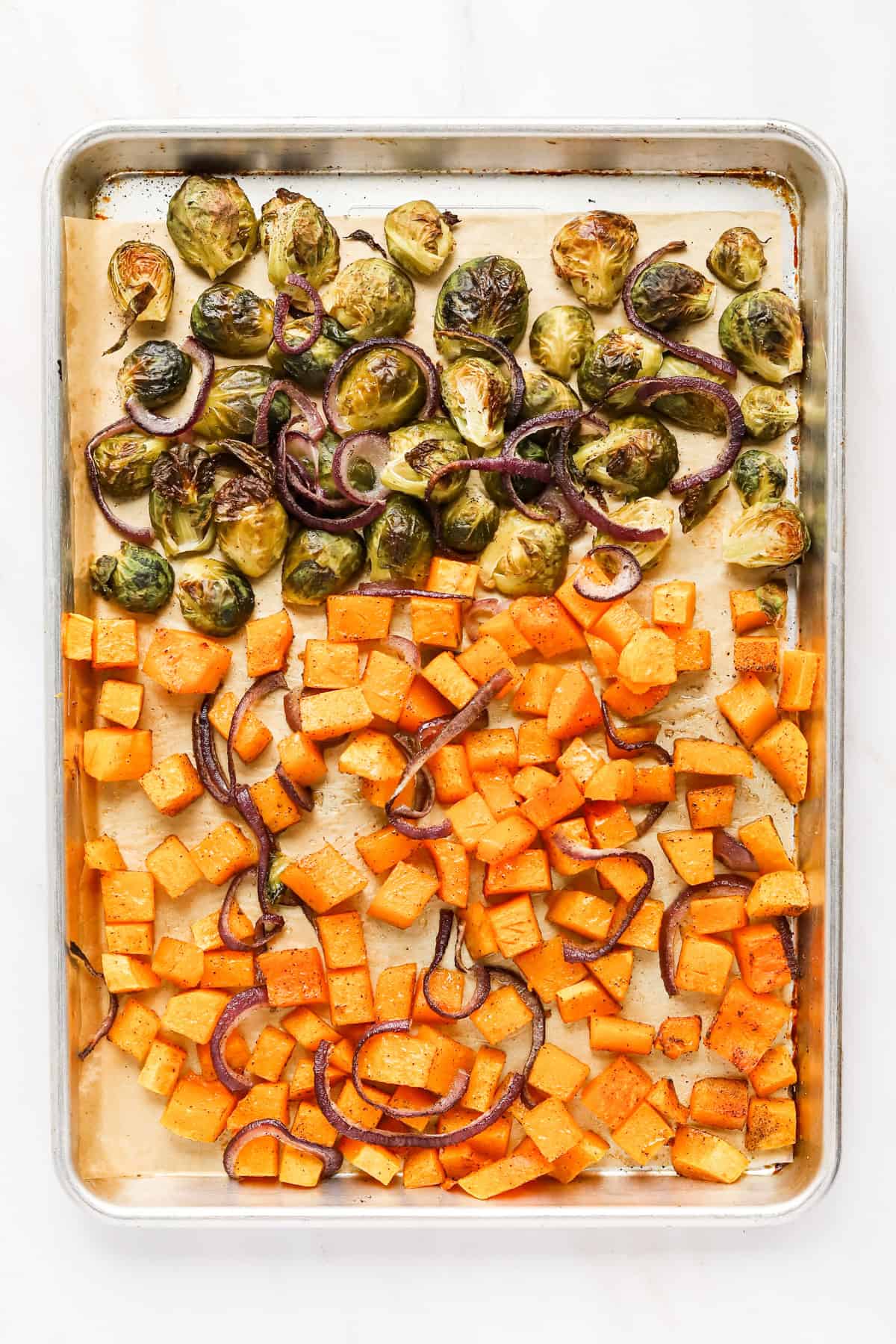 Roasted brussels sprouts, butternut squash and red onion on a sheet pan.