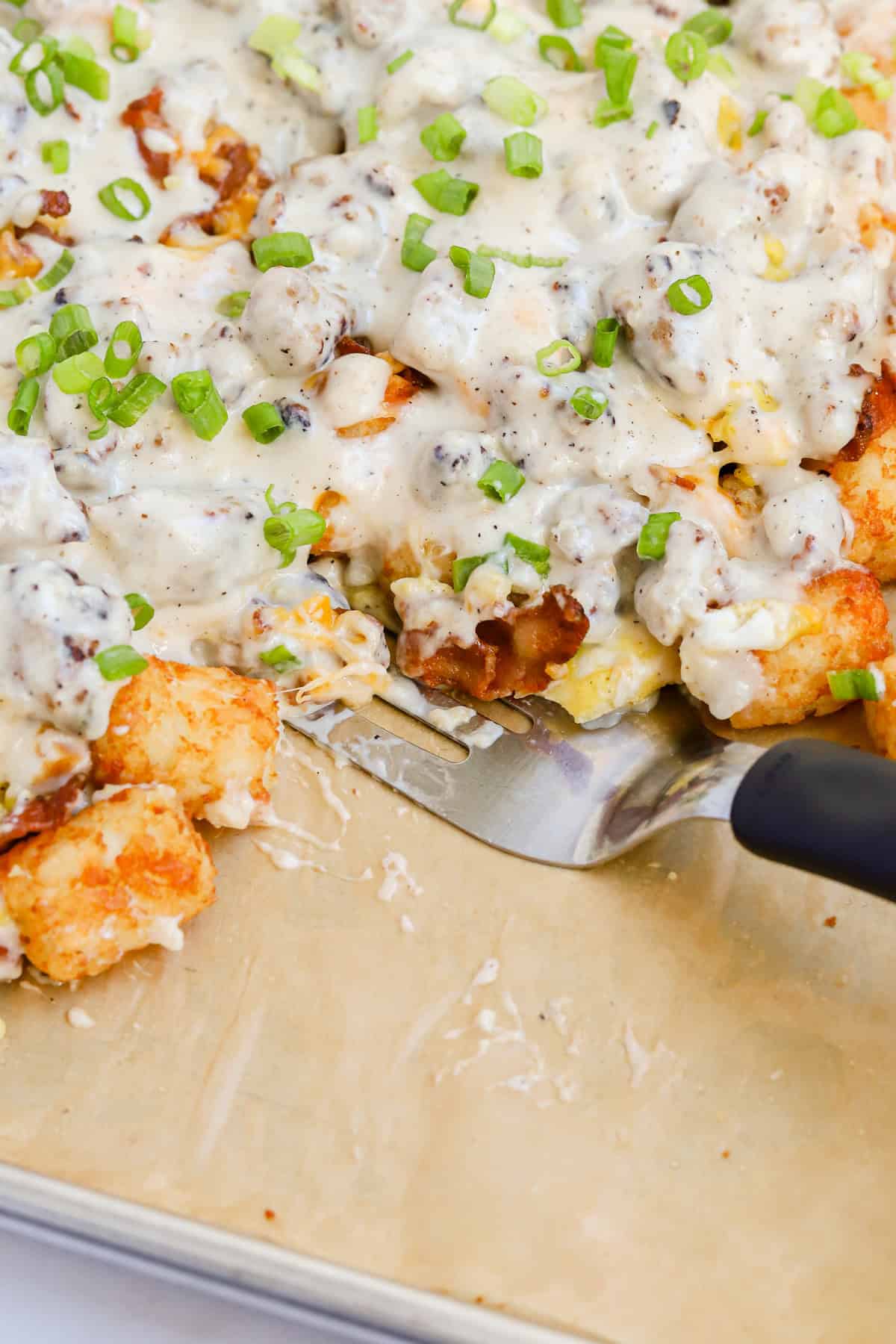 Breakfast totchos on sheet pan with metal spatula.