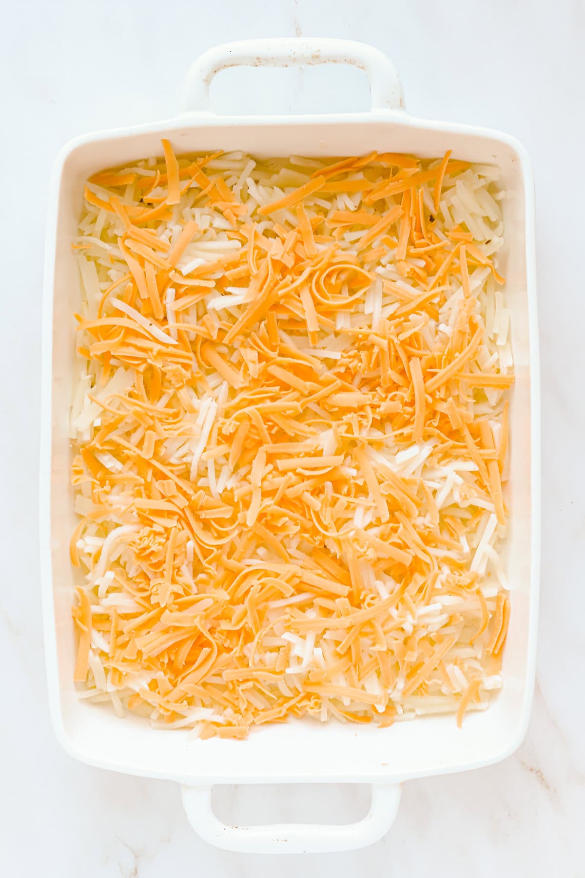Overhead view of hash browns and shredded cheese in 9x13 baking dish.