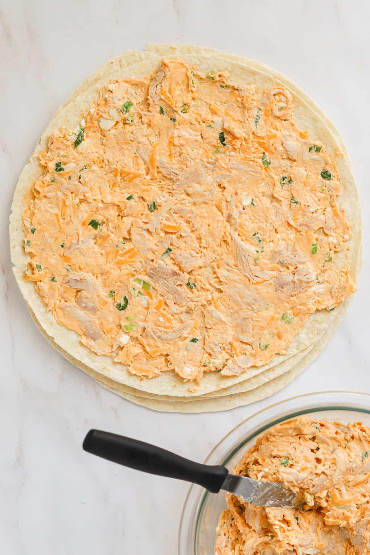 Buffalo chicken filling spread over flour tortilla