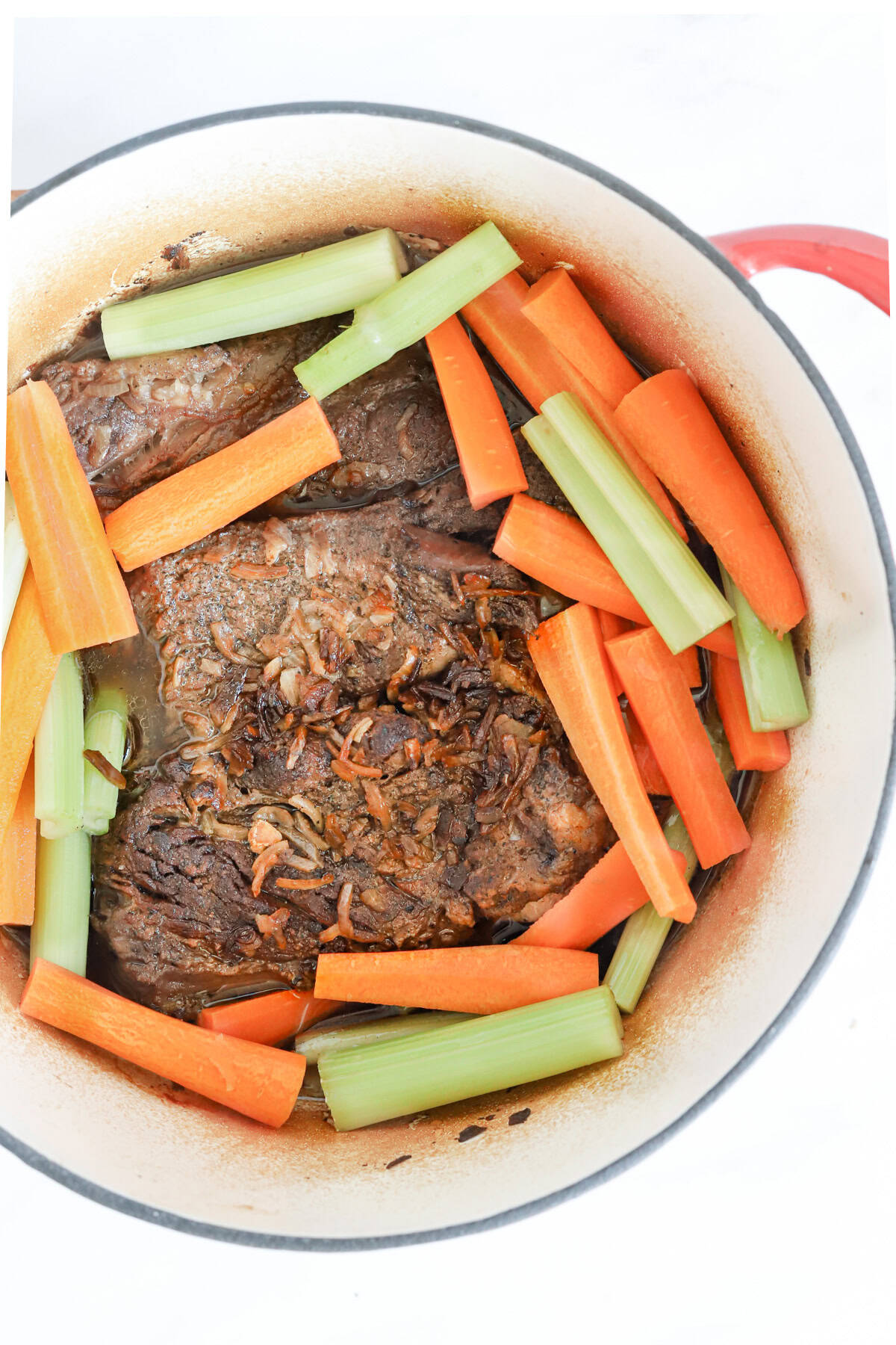 Carrot and celery sticks added to the pot roast in the dutch oven.
