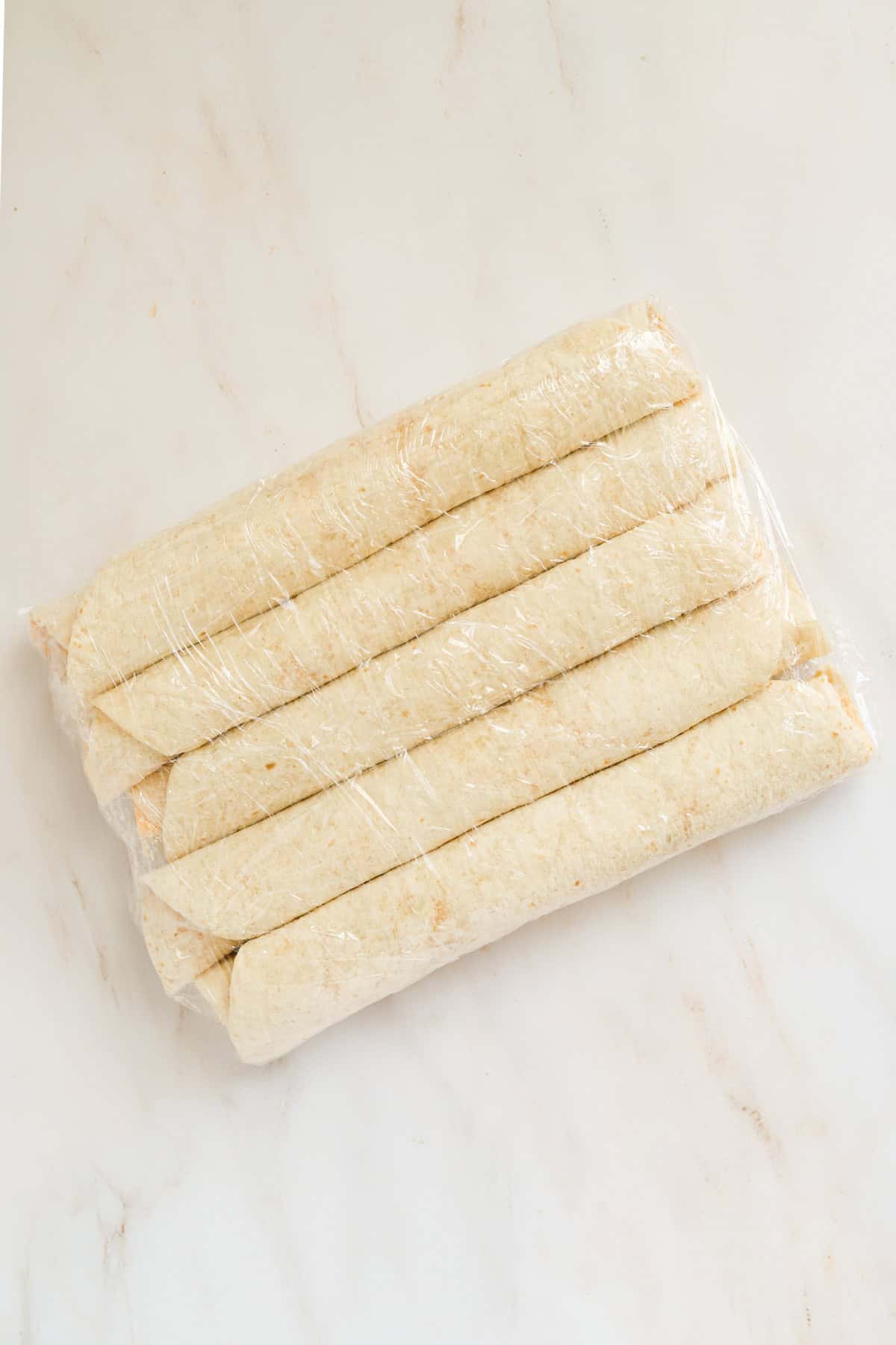 Five tortillas rolled up and wrapped in plastic wrap.